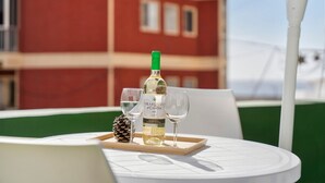 Una mesa con una botella de vino, dos copas y una piña en una bandeja, colocada al aire libre con un edificio de fondo.