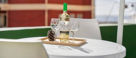Une table avec une bouteille de vin, deux verres et une pomme de pin sur un plateau, le tout installé à l’extérieur, avec un bâtiment en arrière-plan.