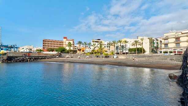 Zona costera con edificios, una playa y agua tranquila.