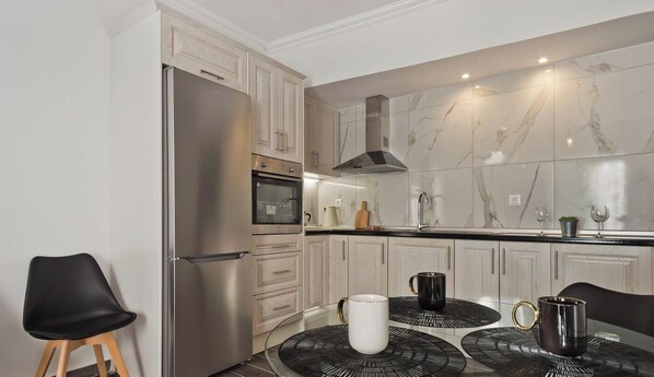 A modern kitchen with a built-in oven, stainless steel refrigerator, and marble backsplash. - Apartment 'Helios  1' with Sea View, Wi-Fi and Air Conditioning (Karpathos)