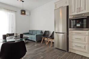 A modern kitchen with a stainless steel refrigerator, wooden cabinets, a glass dining table with chairs, and a hanging pendant light. - Apartment 'Helios  1' with Sea View, Wi-Fi and Air Conditioning (Karpathos)