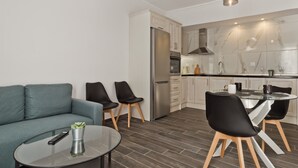 Un salon moderne avec un canapé, des fauteuils, une table basse en verre et une télécommande.