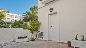 Un bâtiment blanc avec une porte, un luminaire fixé au mur et un petit arbre.
