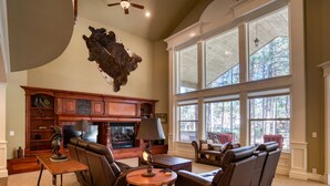 A spacious living room with leather sofas, a fireplace, and large windows offering a view of trees. - Luxury Family Retreat w/ Views, Golf: Fore Seasons (Pinetop)
