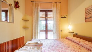 Una habitación de hotel con cama, ventana con cortinas, lámpara de pared y espejo.