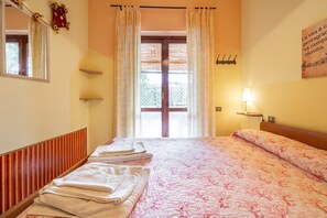 Une chambre d’hôtel avec un lit, une fenêtre avec des rideaux, une lampe fixée au mur et un miroir.