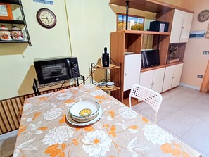 A dining area with a table set for two, a microwave, and a cabinet with various items. - Holiday Home 'Pentagramma Apartment Villasimius' with Private Terrace and Wi-Fi (Villasimius)