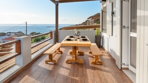 Una mesa de madera con bancos en un balcón con vista al mar.