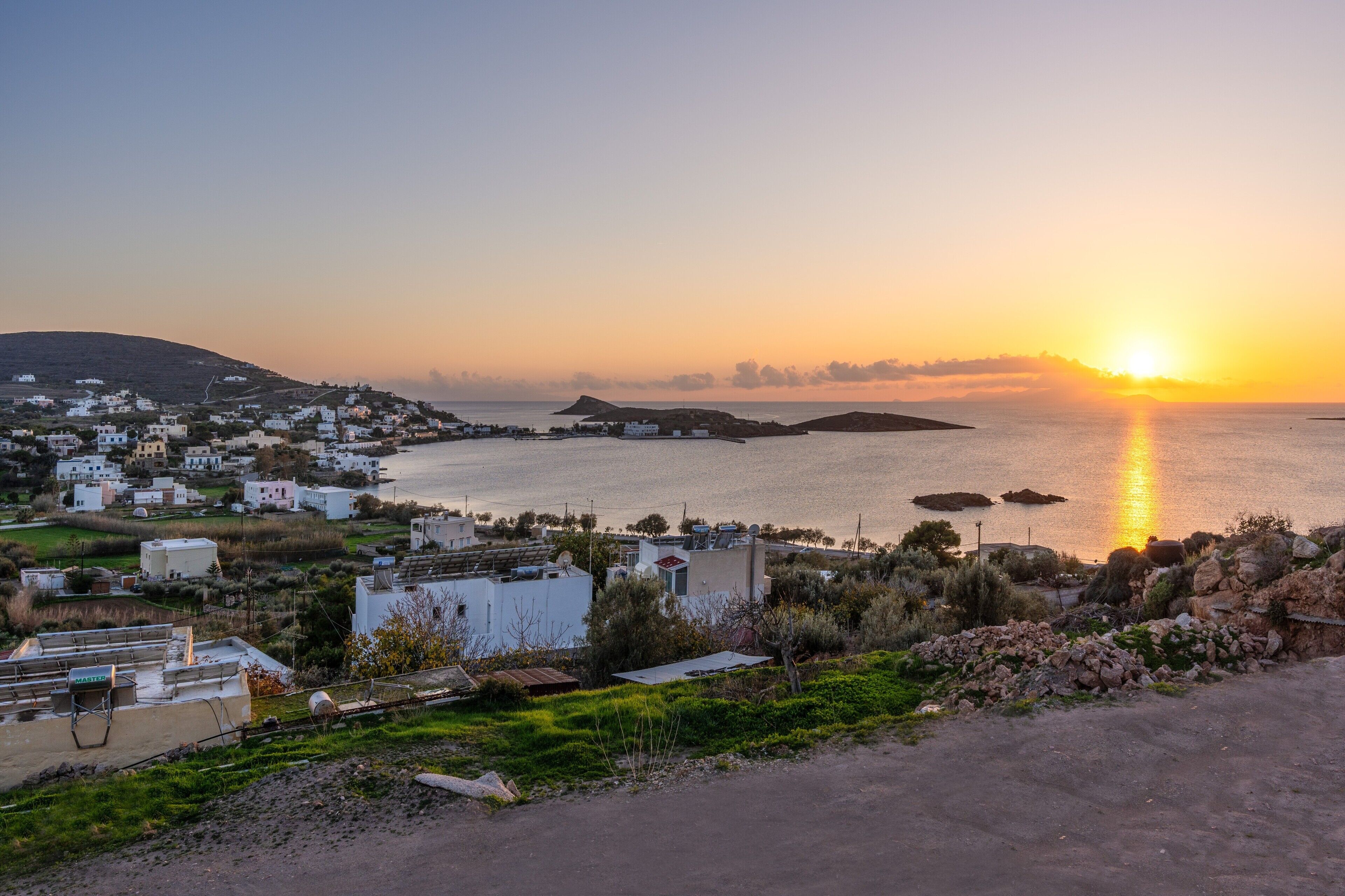 Une ville côtière avec des bâtiments, une route et un coucher de soleil sur la mer.