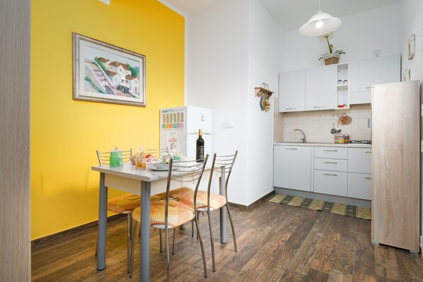 A compact kitchen with white cabinets, a dining table with chairs, a refrigerator, and a hanging plant.