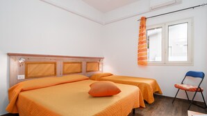 Een kamer met twee bedden, een raam met gordijnen, een stoel en een houten hoofdbord.