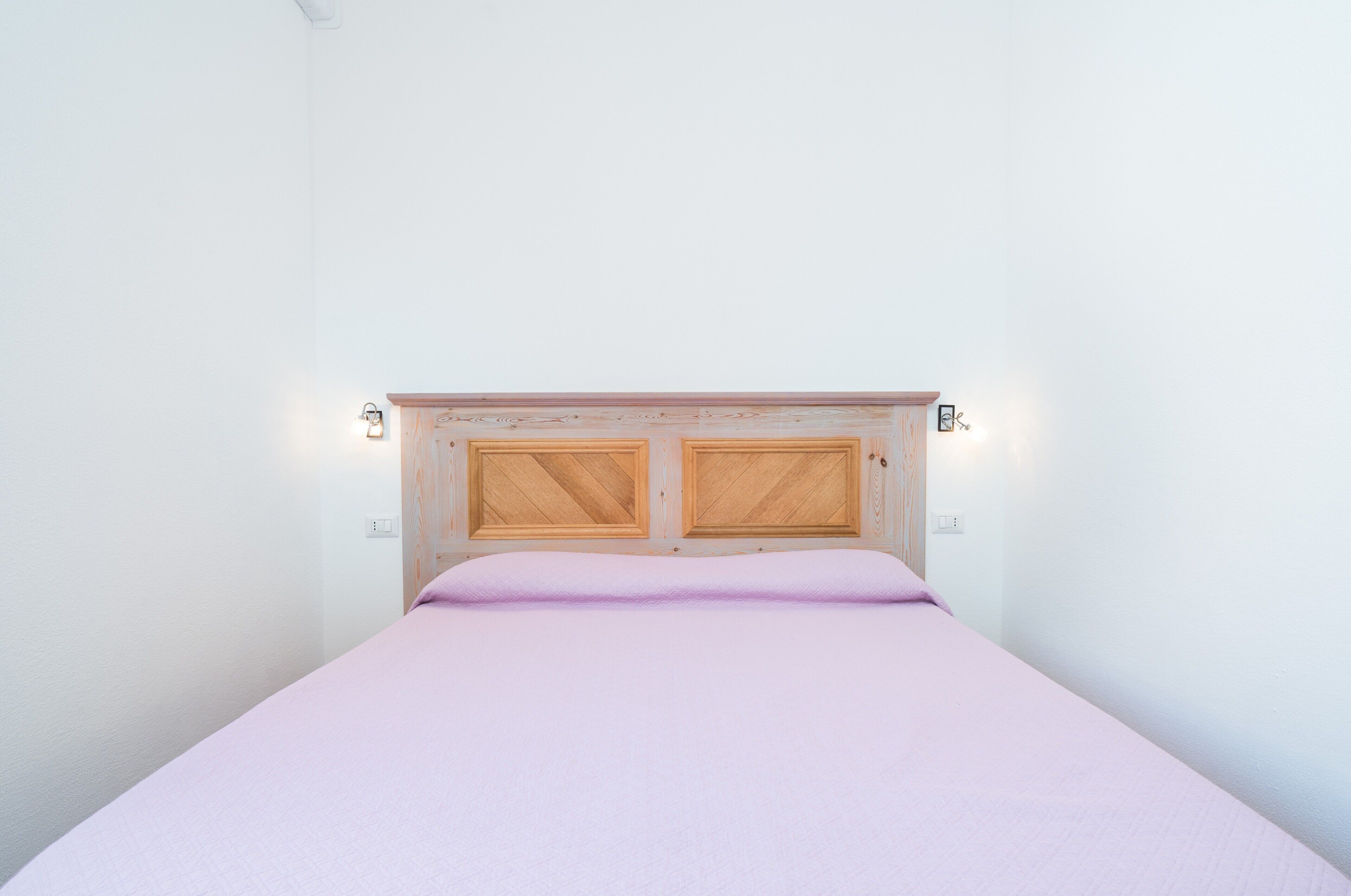 A bed with a wooden headboard, two wall-mounted lights, and a plain white wall.