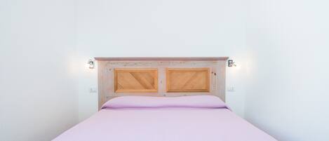 A bed with a wooden headboard, two wall-mounted lights, and a plain white wall.