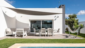 A modern outdoor pool area with a white building, a glass door, and a hammock.