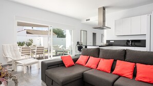 A modern living room with a grey sectional sofa, white chairs, and a red accent pillow.