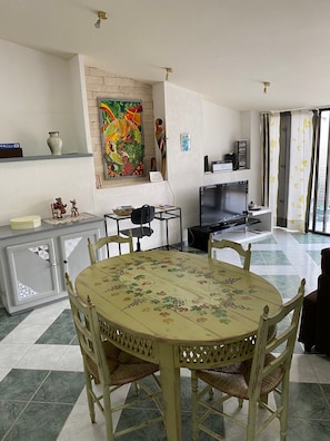 Un coin repas avec une table ronde, des chaises, un téléviseur et un tableau accroché au mur.
