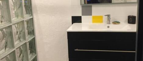 Une salle de bain avec une douche à parois de verre, un lavabo blanc avec un distributeur de savon jaune et un meuble-lavabo noir doté de tiroirs.