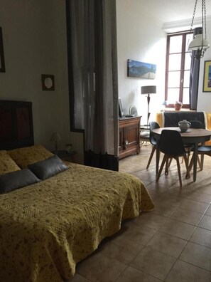 A bedroom with a bed, a dining area with a table and chairs, a lamp, and a window. - Apartment 'Gîte De La Chatiere' with Mountain View, Private Terrace and Wi-Fi (Villefort)