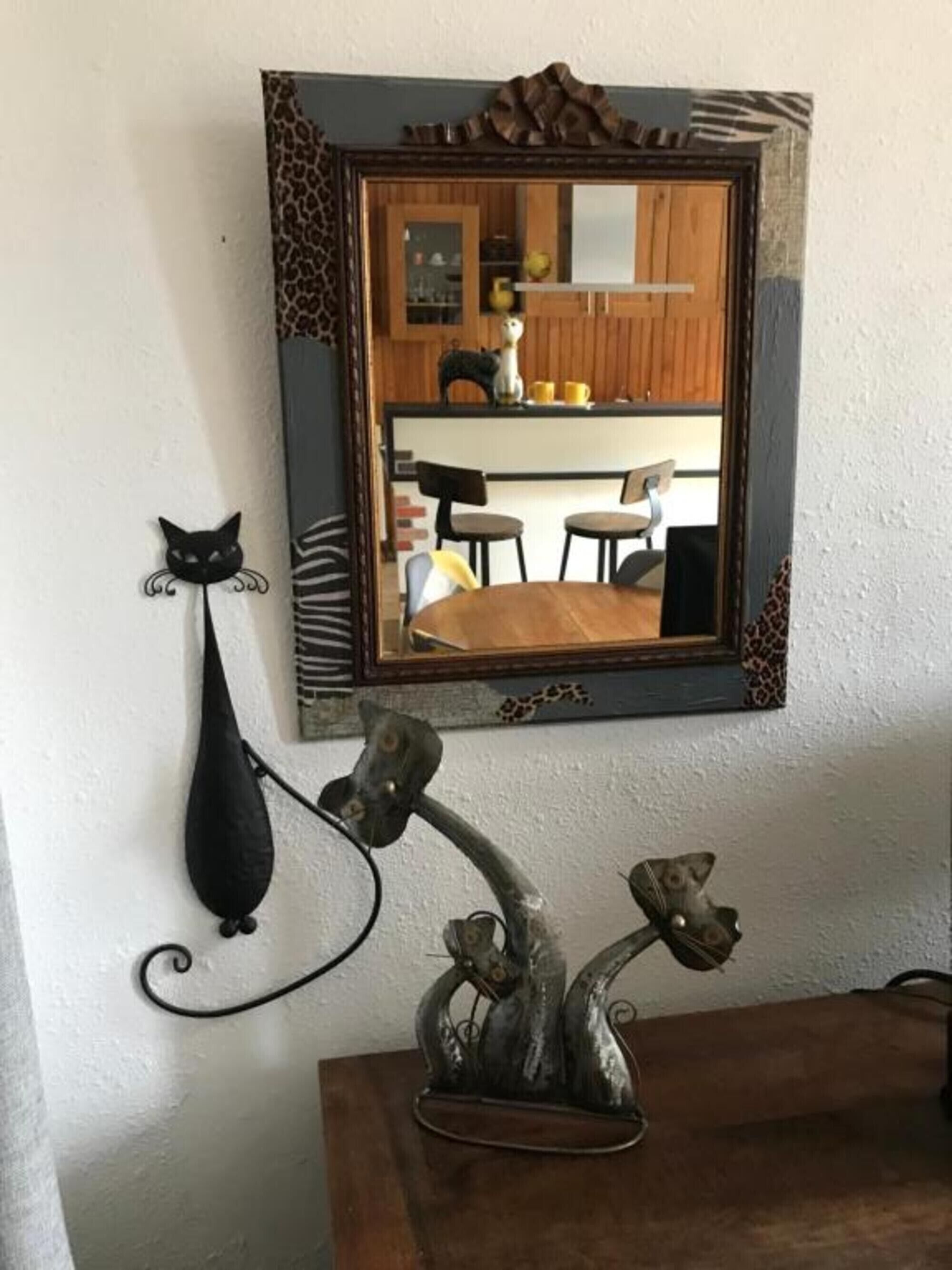 Un miroir avec un cadre décoratif, un crochet en forme de chat noir et une sculpture en métal accrochée au mur.