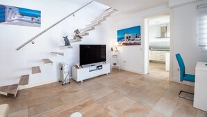 Un soggiorno moderno con una televisione a schermo piatto, una scala e vista sulla cucina.
