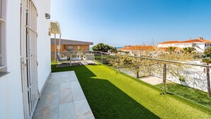 Un balcone abitativo con vista su un prato verde, un edificio bianco e un cielo sereno.