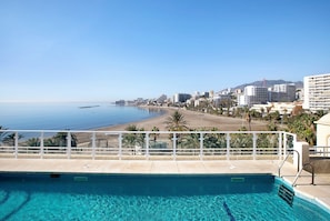 A pool with clear water, a beach, and buildings in the background.