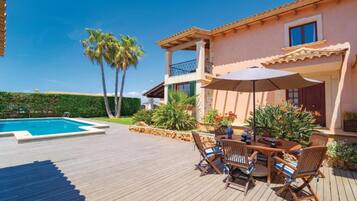 Ein Poolbereich mit Holzterrasse, Gartenmöbeln und einem zweistöckigen Gebäude mit Balkonen.