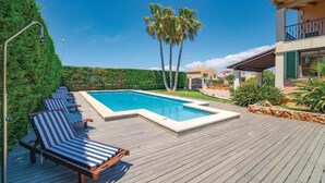 Ein Schwimmbecken mit Liegestühlen, Palmen und einem Gebäude mit Balkon.