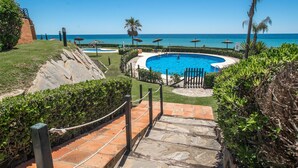 Una piscina con vistas al océano, rodeada de palmeras y sombrillas.