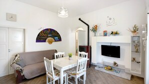 A living room with a white sofa, a dining table with chairs, a flat-screen TV mounted on the wall, and a fireplace. - Apartment 'Bella Veduta Luna' with Sea and Mountain Views, Wi-Fi, and Air Conditioning (Agerola)