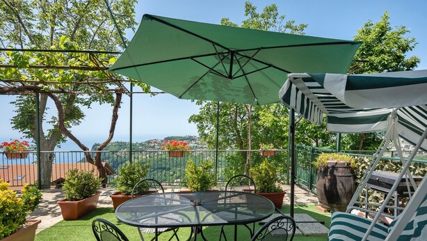 A patio with a table and chairs, a green umbrella, and potted plants. - Apartment 'Bella Veduta Luna' with Sea and Mountain Views, Wi-Fi, and Air Conditioning (Agerola)