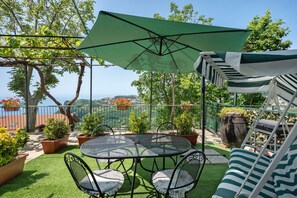 Un patio con una mesa y sillas, un paraguas verde y plantas en macetas.