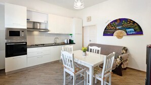 A modern kitchen with white cabinetry, a microwave, stove, and a dining area with a table and chairs. - Apartment 'Bella Veduta Luna' with Sea and Mountain Views, Wi-Fi, and Air Conditioning (Agerola)