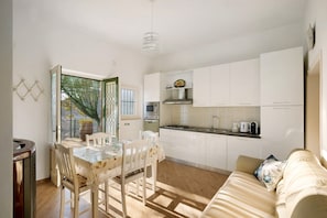 A modern kitchen with white cabinets, a dining table with chairs, and a sofa in a bright living area with a view through a glass door. - Apartment 'Bella Veduta' with Sea and Mountain Views (Agerola)