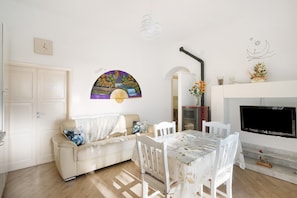 A living room with a sofa, dining table, chairs, a TV, a fireplace, and a wall clock. - Apartment 'Bella Veduta' with Sea and Mountain Views (Agerola)