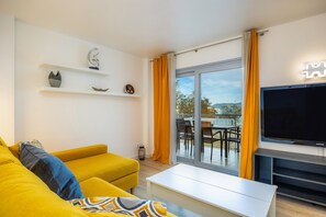 A modern living room with a sofa, television, and a balcony with outdoor furniture.