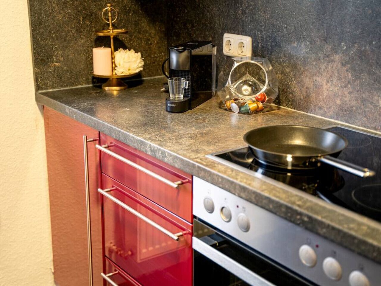 A kitchen with a stove, coffee maker, and a candle on the countertop.