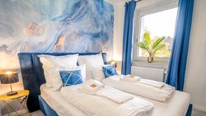 Ein Doppelbett mit weißen Leinen, einem blauen Kopfteil und einer Marmor-Wandmalerei.