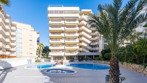 A multi-story hotel with a swimming pool, palm trees, and a well-maintained lawn. - Apartment 'Apartamento Ct' with Shared Pool, Wi-Fi and Air Conditioning (Salou)