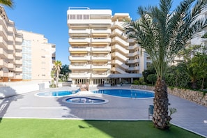 A multi-story hotel with a swimming pool, palm trees, and a well-maintained lawn.