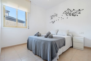 A bedroom with a bed, a nightstand, a window, and a wall decal.