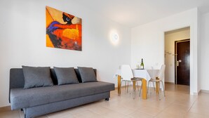 A modern living room with a grey sofa, a dining table with chairs, a painting on the wall, and a door in the background. - Apartment 'Apartamento Ct' with Shared Pool, Wi-Fi and Air Conditioning (Salou)