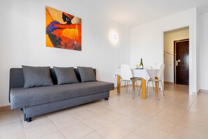 Un salon moderne avec un canapé gris, une table à manger et des chaises, un tableau accroché au mur et une porte visible au fond.