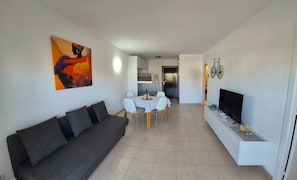 A living room with a sofa, a dining table with chairs, a TV, and a painting on the wall.