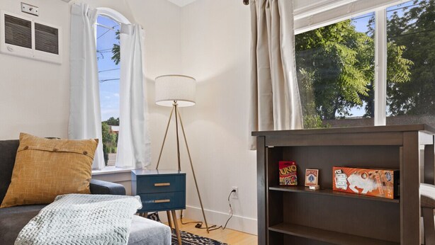 A cozy room with a grey sofa, a patterned throw blanket, a blue floor lamp, and a bookshelf with board games. - Good 2 Go at L Rancho Court (Spearfish)