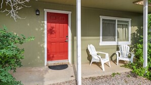 A red door, two white chairs, and a window on a house facade. - Good 2 Go at L Rancho Court (Spearfish)