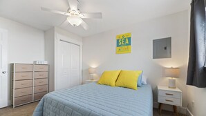 A bedroom with a bed, a ceiling fan, a nightstand with a lamp, a storage unit, and a sign on the wall. - Good 2 Go at L Rancho Court (Spearfish)