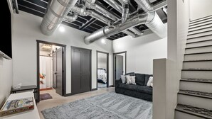 A modern living room with a grey sofa, a patterned rug, and a staircase with a metal railing. - Crate Escape at Terry Peak (Lead)