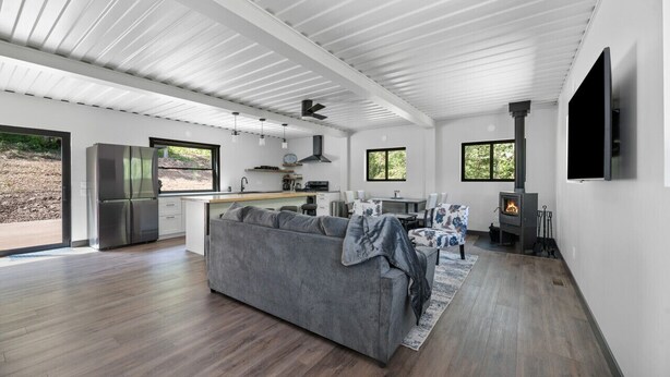A modern kitchen with a central island, a dining area with a table and chairs, a gray sofa, and a fireplace. - Crate Escape at Terry Peak (Lead)