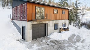A modern cabin with a large garage, wooden exterior, and a view of the surrounding forest. - Crate Escape at Terry Peak (Lead)